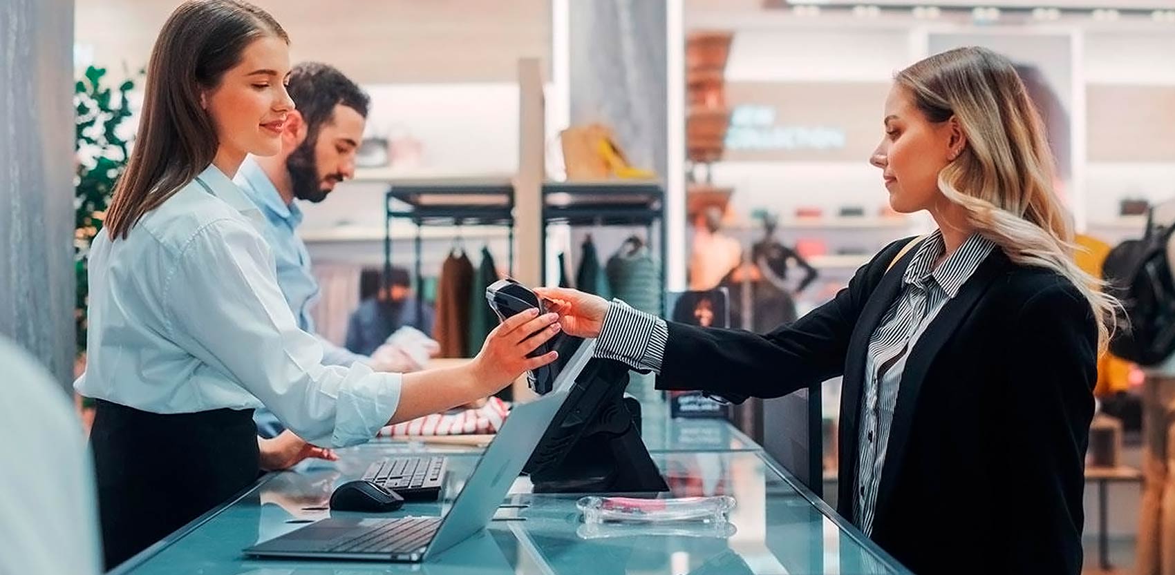 Ofrece pagos rápidos y sin contacto para mejorar la experiencia de tus clientes Cliente realizando pago contactless con tarjeta en tienda de ropa, atendida por cajera con terminal POS