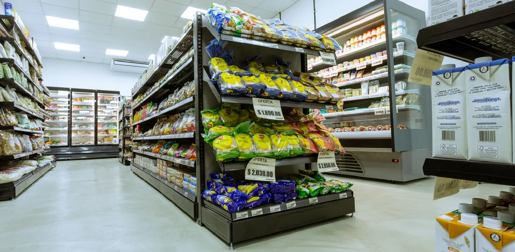 Pasillo central de supermercado con góndolas metálicas y exhibiciones promocionales organizadas por categorías
