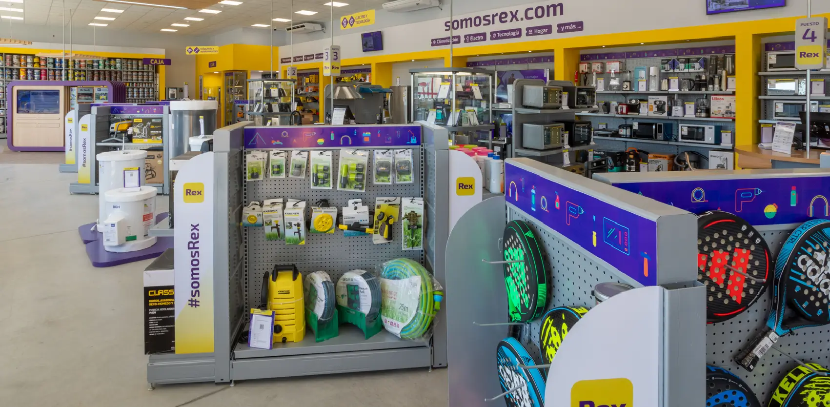 Tienda de electrodomésticos con góndolas metálicas y exhibidores centrales para productos tecnológicos